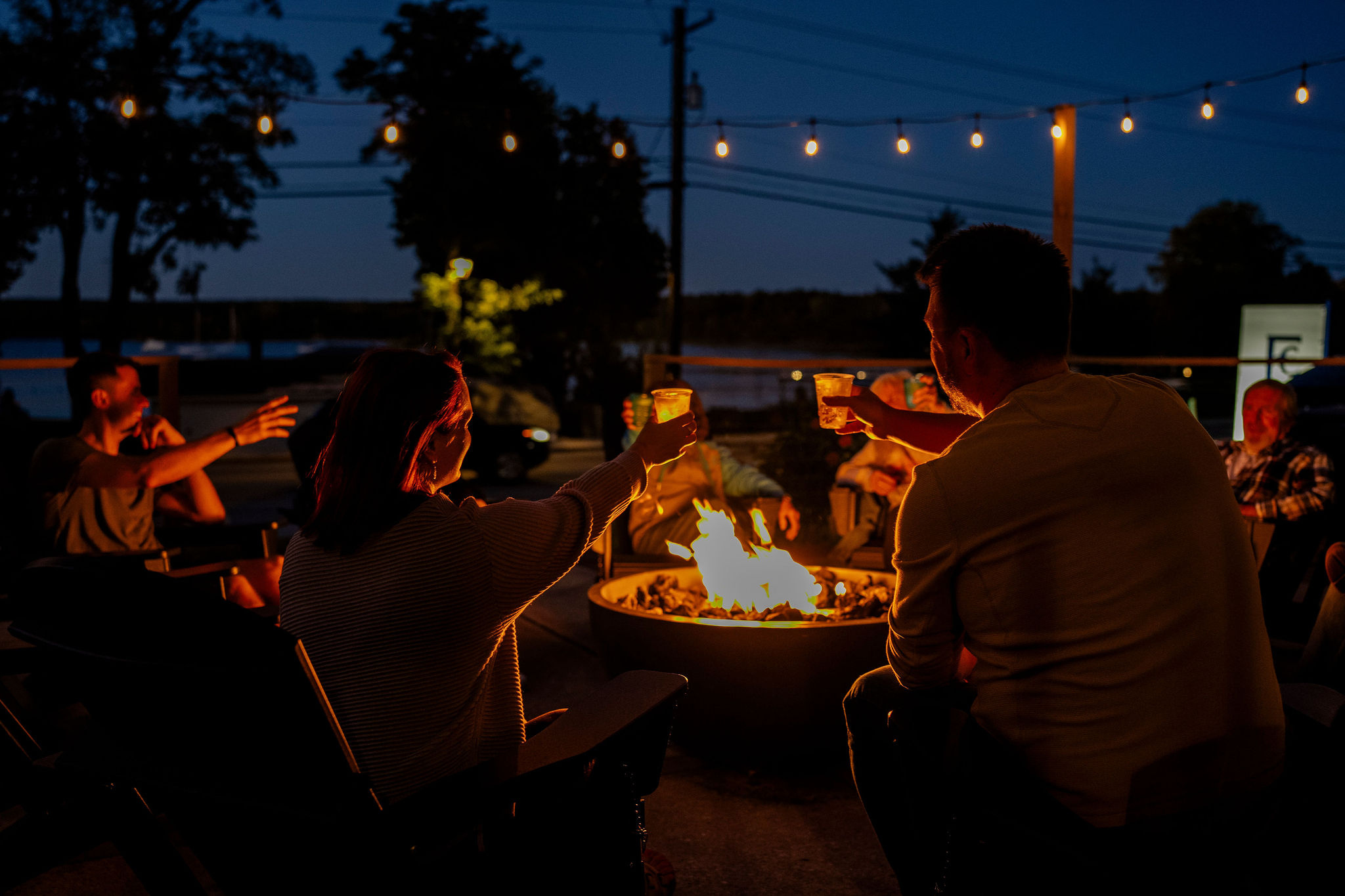 Group toasting around outdoor campfire at night.