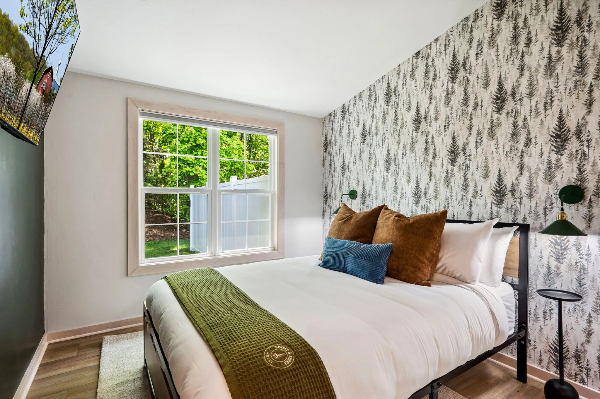 Cozy bedroom with forest-themed wallpaper and window view.
