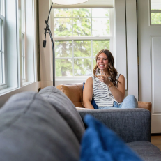 Smiling person sitting on a couch near window.